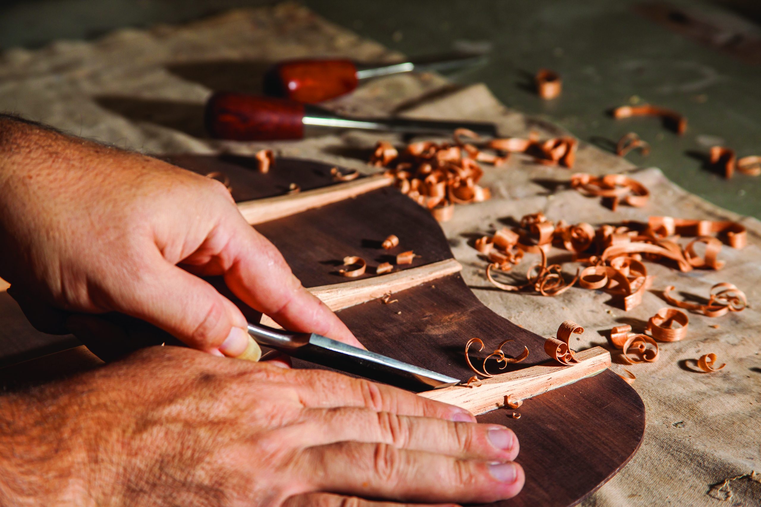 hands cutting away at excess wood on the body of a violin